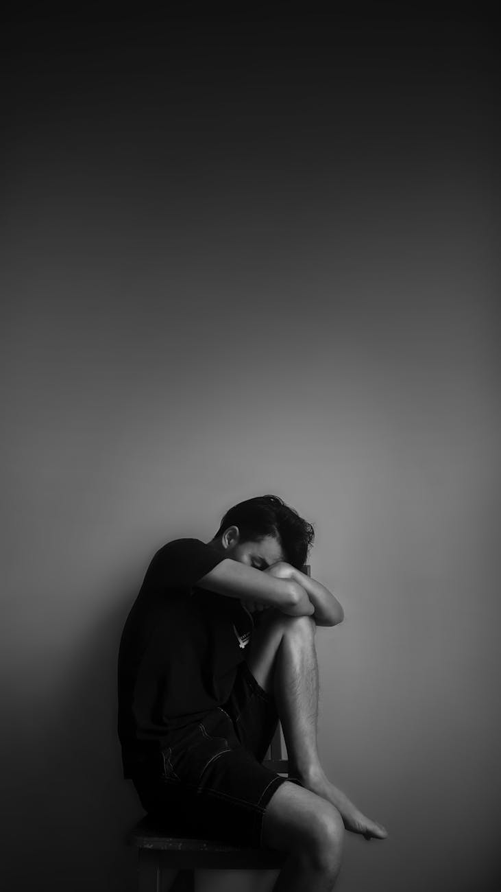 grayscale photography of man sitting beside wall